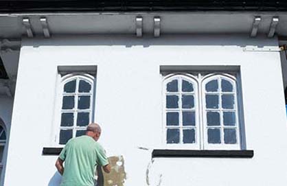 A painter adding color to a white building's exterior.