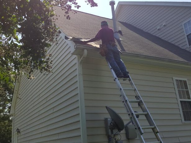 A man on a ladder cleaning the roof of a house.