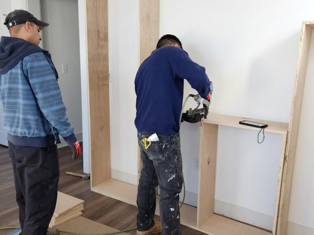 Two workers renovating a wall in a room.