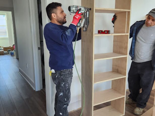 Two men putting together a bookcase inside a room.